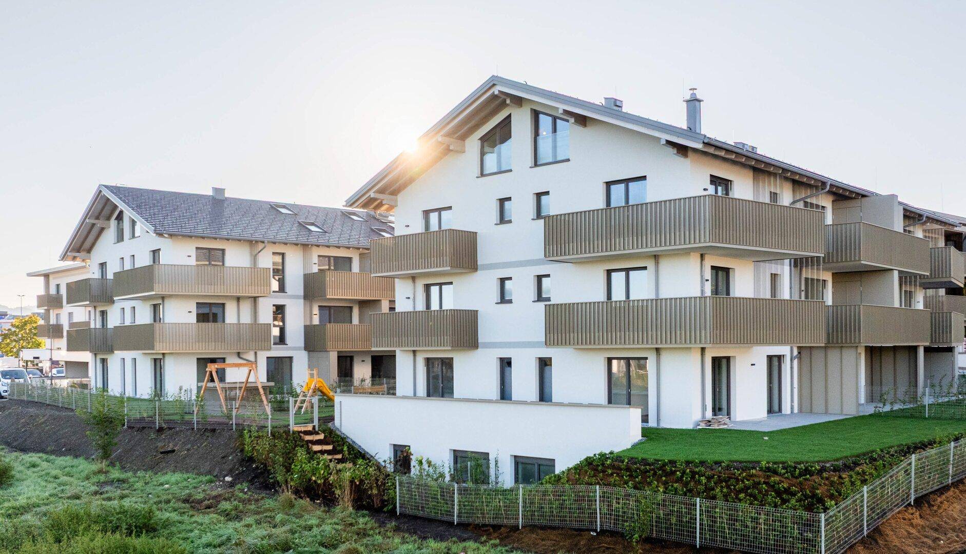 Moderne Wohnanlage mit Balkonen, Grünflächen und einem Kinderspielplatz.