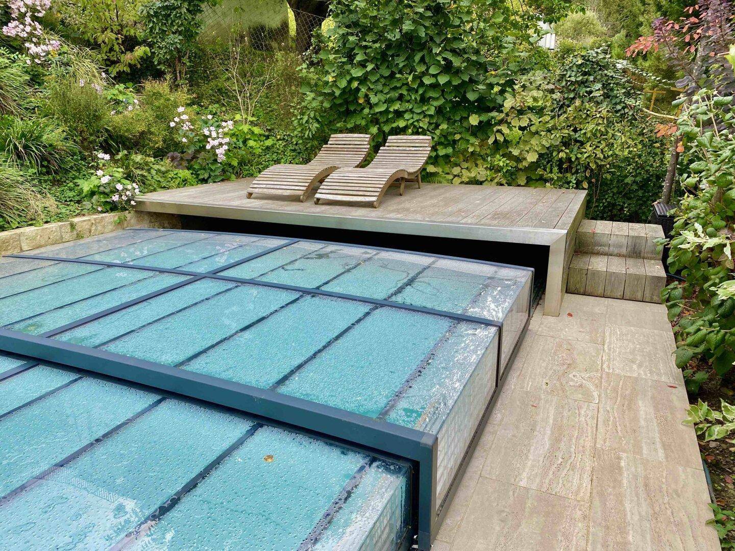Eingebetteter Poolbereich mit Holzdeck und Liegestühlen, umgeben von üppigem Grün.