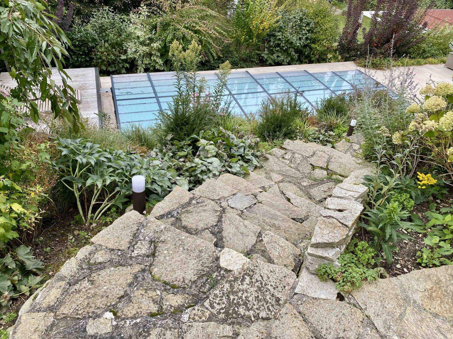 Steintreppe führt durch den terrassierten Garten zum Poolbereich mit üppiger Bepflanzung.