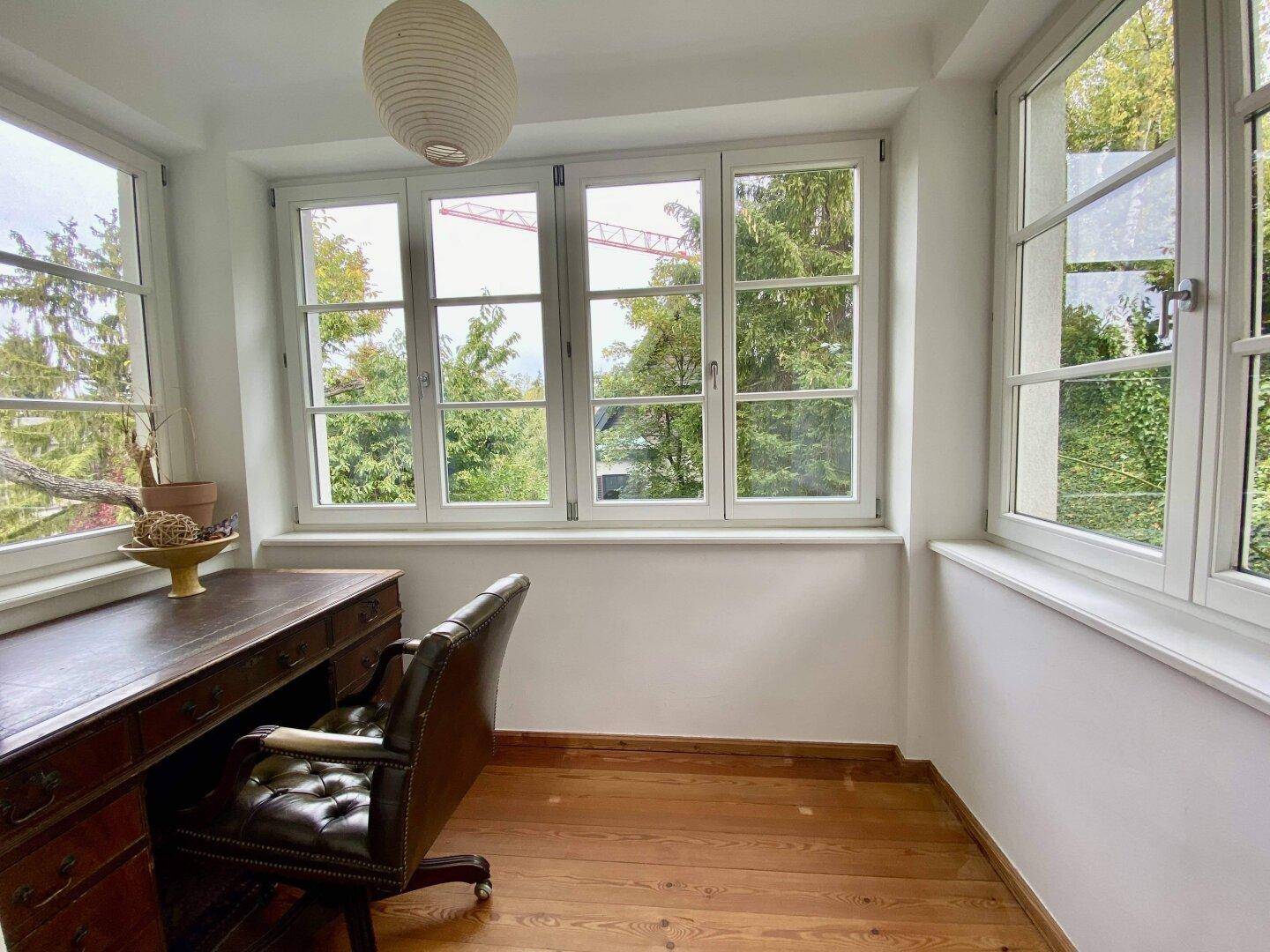 Ruhiges Arbeitszimmer mit Holzboden und weitem Blick über die Baumwipfel.