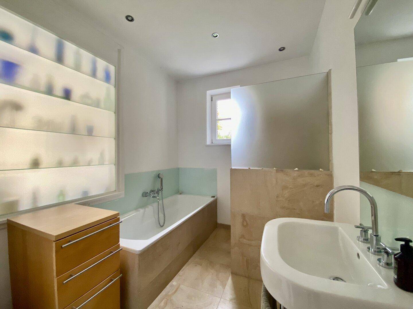 Modernes Badezimmer mit Badewanne, Waschbecken und Fenster für Tageslicht.