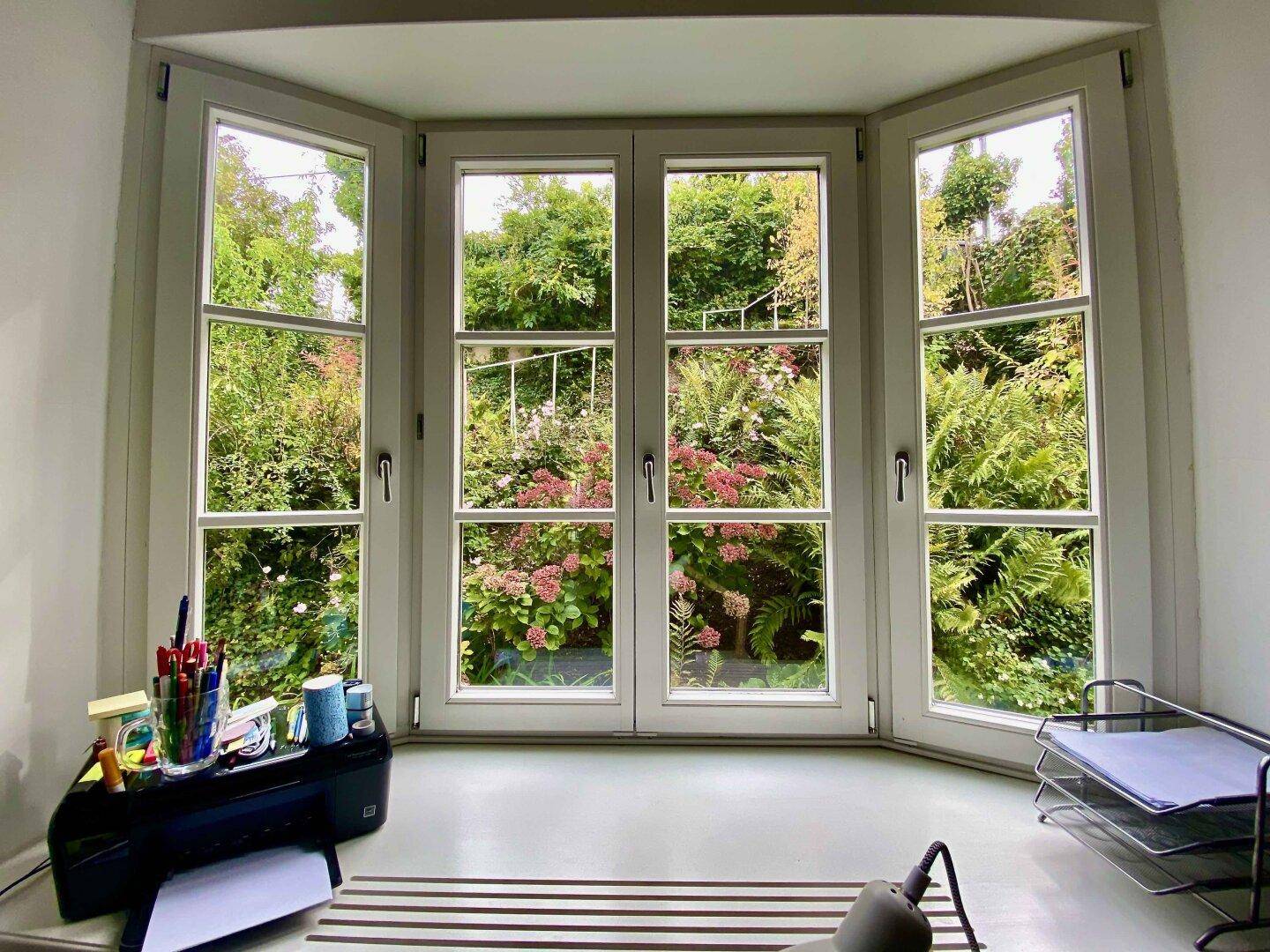 Helles Arbeitszimmer mit Erkerfenstern und Blick in den grünen Garten.