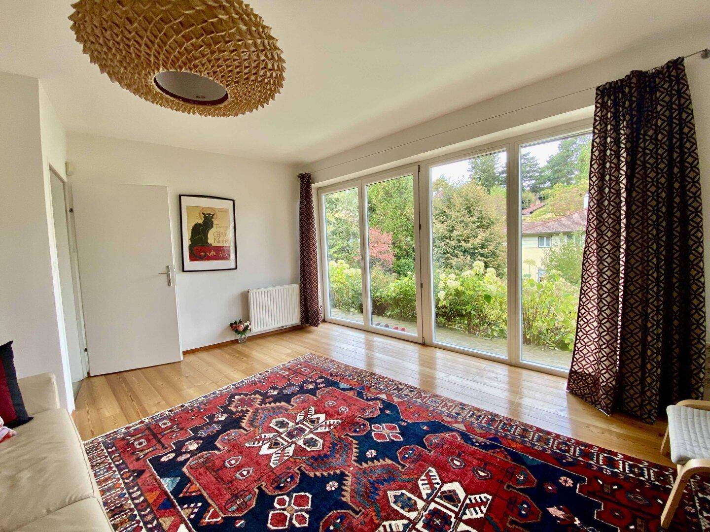 Gemütliches Wohnzimmer mit Holzboden, großem Teppich und Zugang zum Garten.