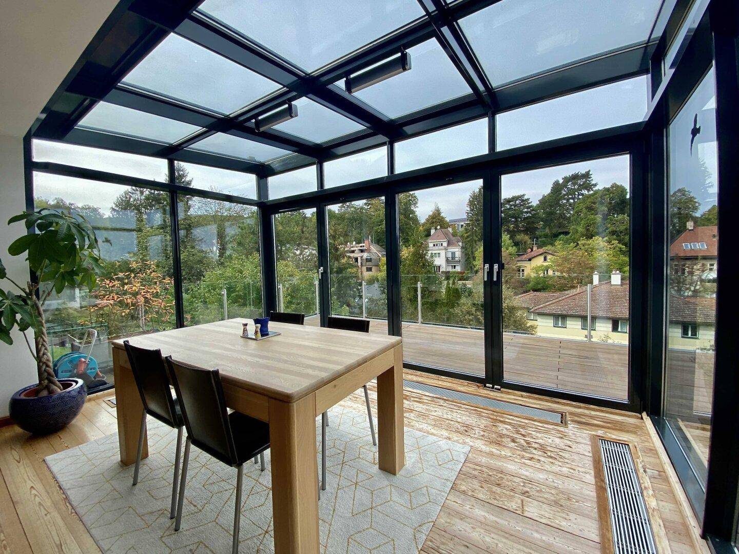 Moderner Essbereich im Wintergarten mit großen Glasflächen und weitem Ausblick.