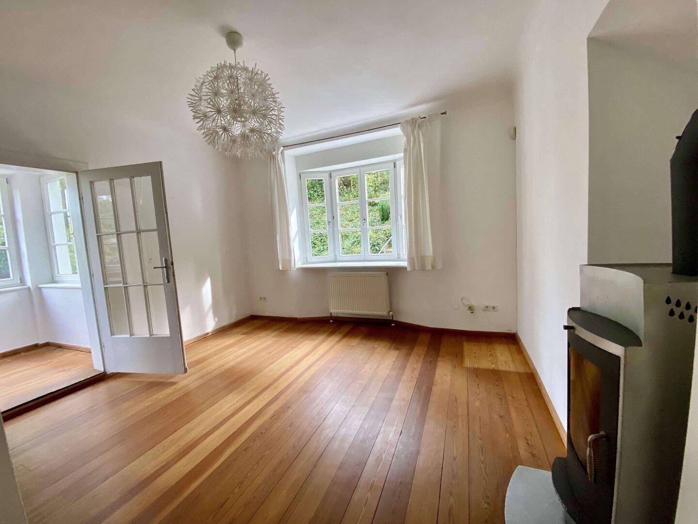 Helles Wohnzimmer mit Holzboden, Kaminofen und Blick ins Grüne.