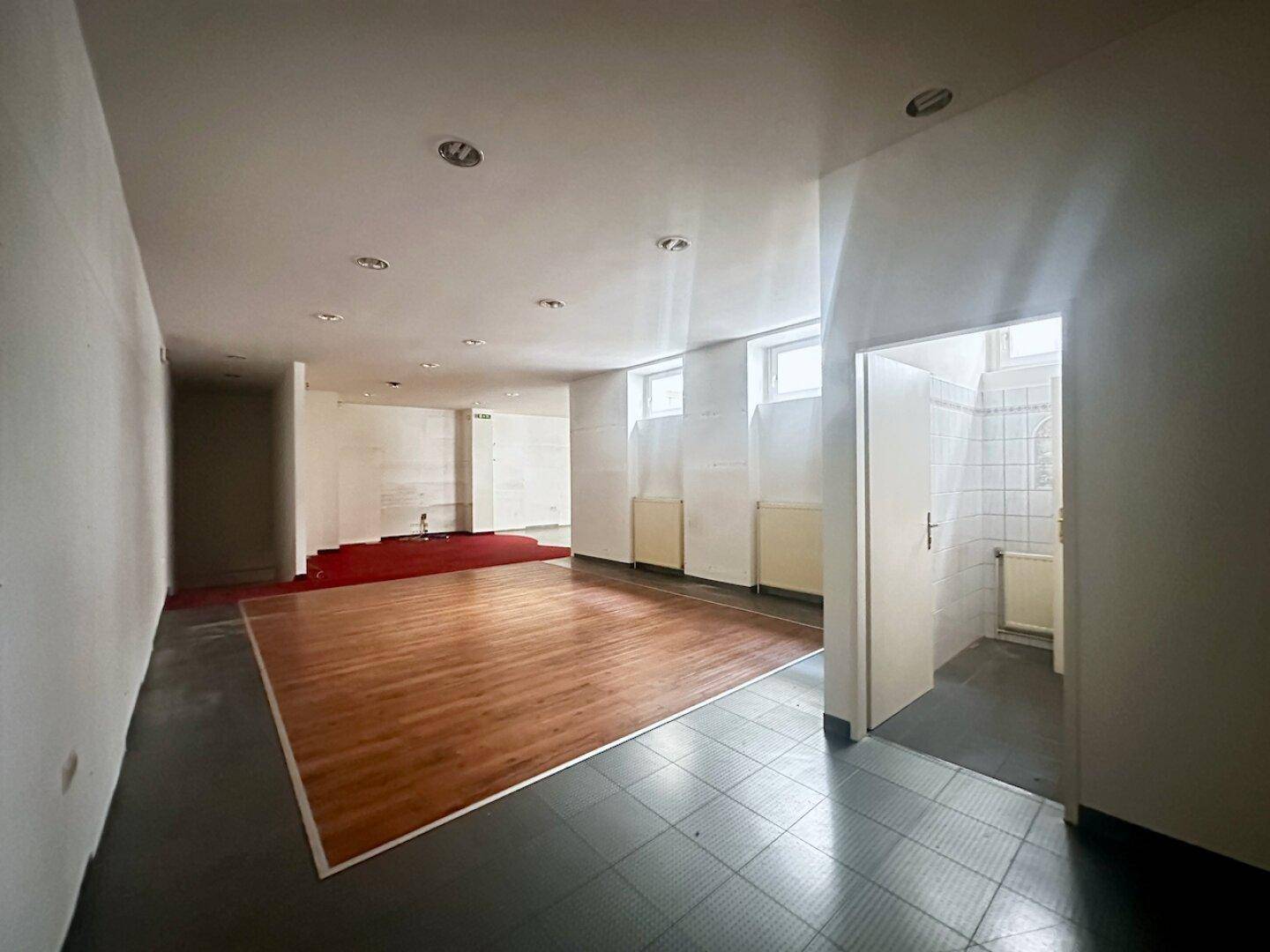 Untergeschossbereich mit Holzboden und Zugang zu einem gefliesten Badezimmer, gut beleuchtet.