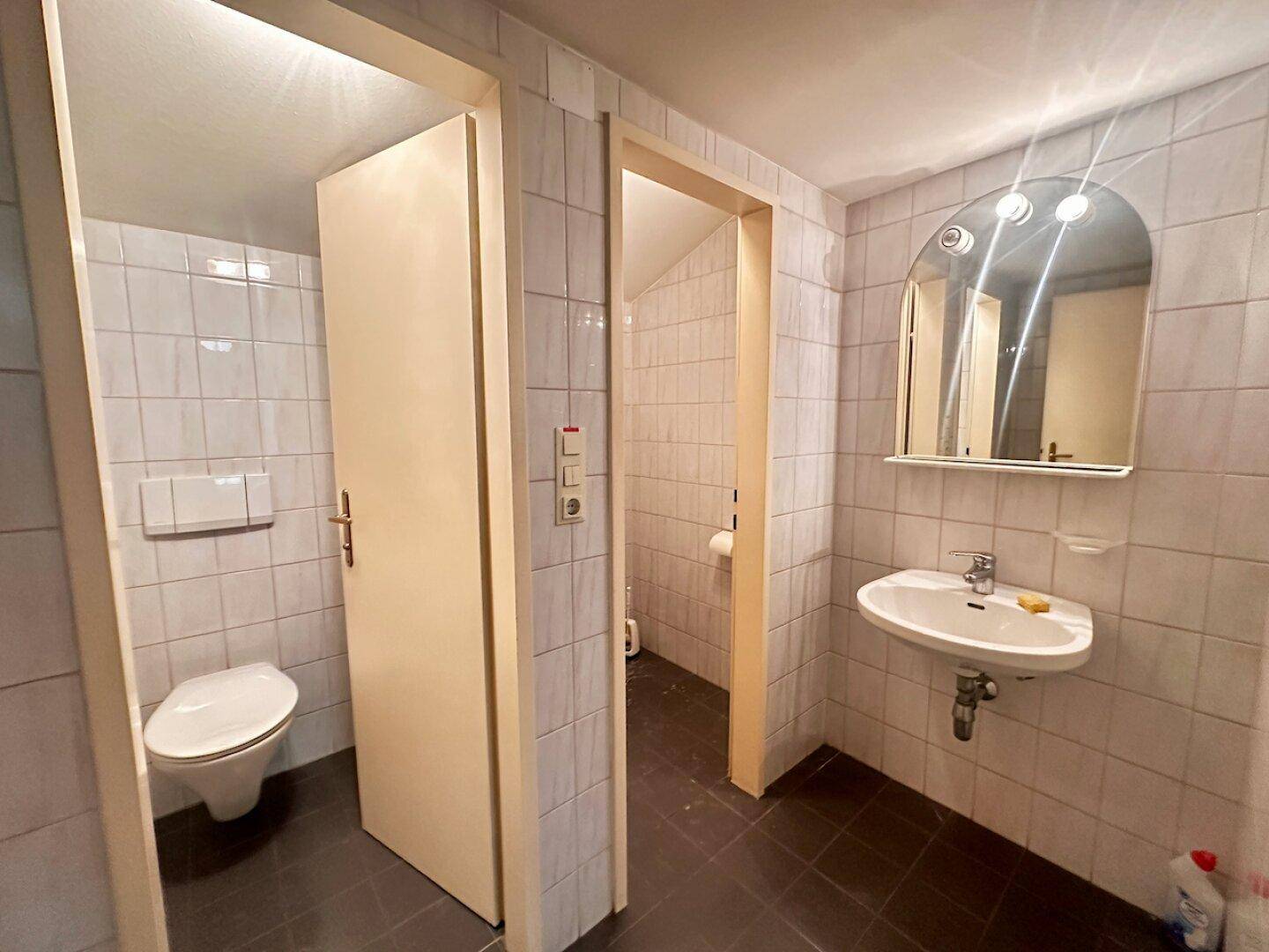Gefliestes Badezimmer mit Toilette, Waschbecken und Spiegel, in gutem, funktionalem Zustand.