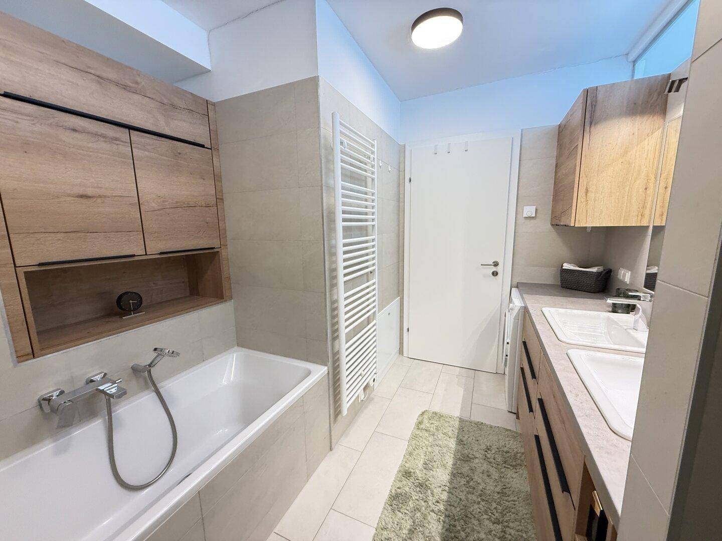 Stilvolles Badezimmer mit Badewanne, Handtuchheizkörper und Holzdetails an den Schränken.