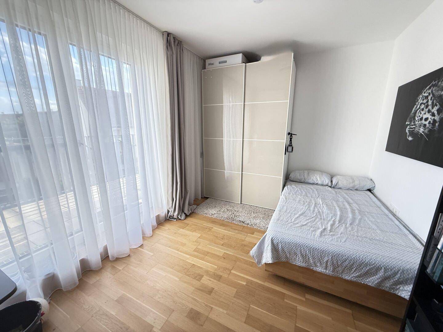 Helles Schlafzimmer mit Einzelbett, Schiebetürenschrank und viel Tageslicht durch große Fenster.