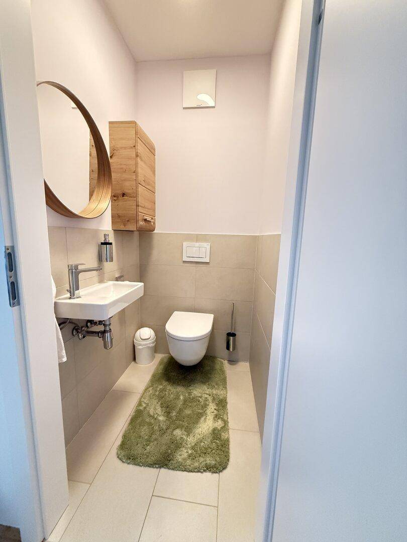 Separates Gäste-WC mit modernem Wand-WC, kleinem Waschbecken und rundem Spiegel.
