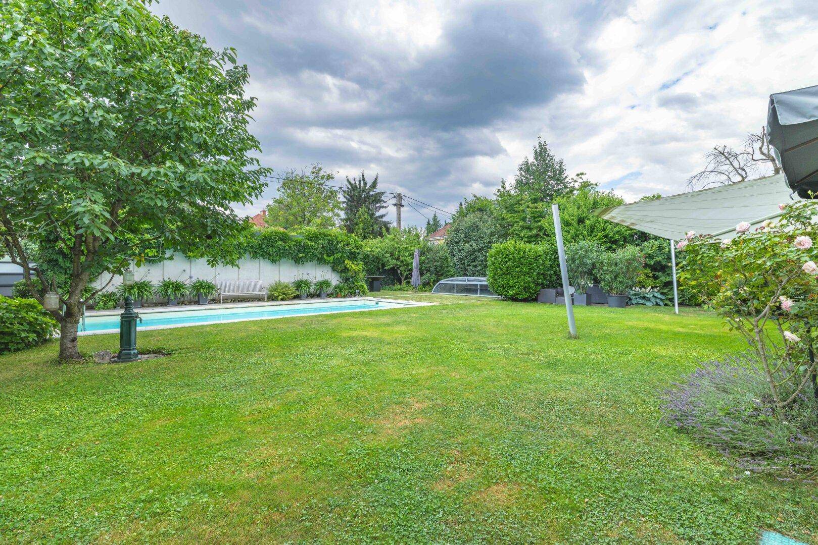 Weitläufiger Garten mit großer Rasenfläche, Bäumen und einem Pool im Hintergrund.