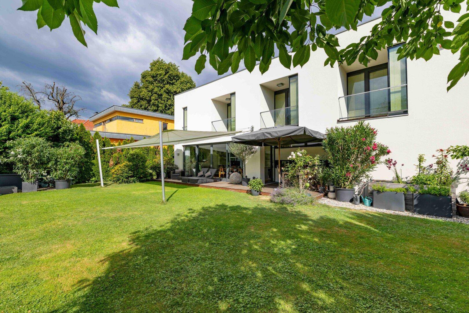 Gepflegter Garten mit Rasenfläche und einer überdachten Holzterrasse am modernen Wohnhaus.