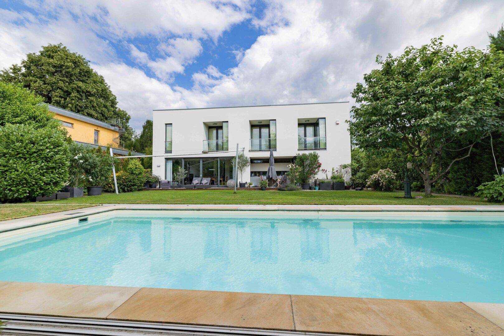 Weitläufiger Garten mit großem Swimmingpool und Blick auf die moderne Hausfassade.