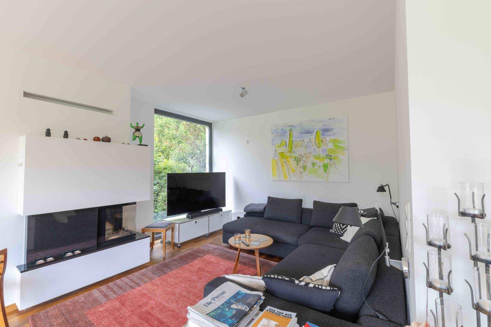 Gemütliches Wohnzimmer mit großem Ecksofa, modernem Kamin und Blick in den Garten.