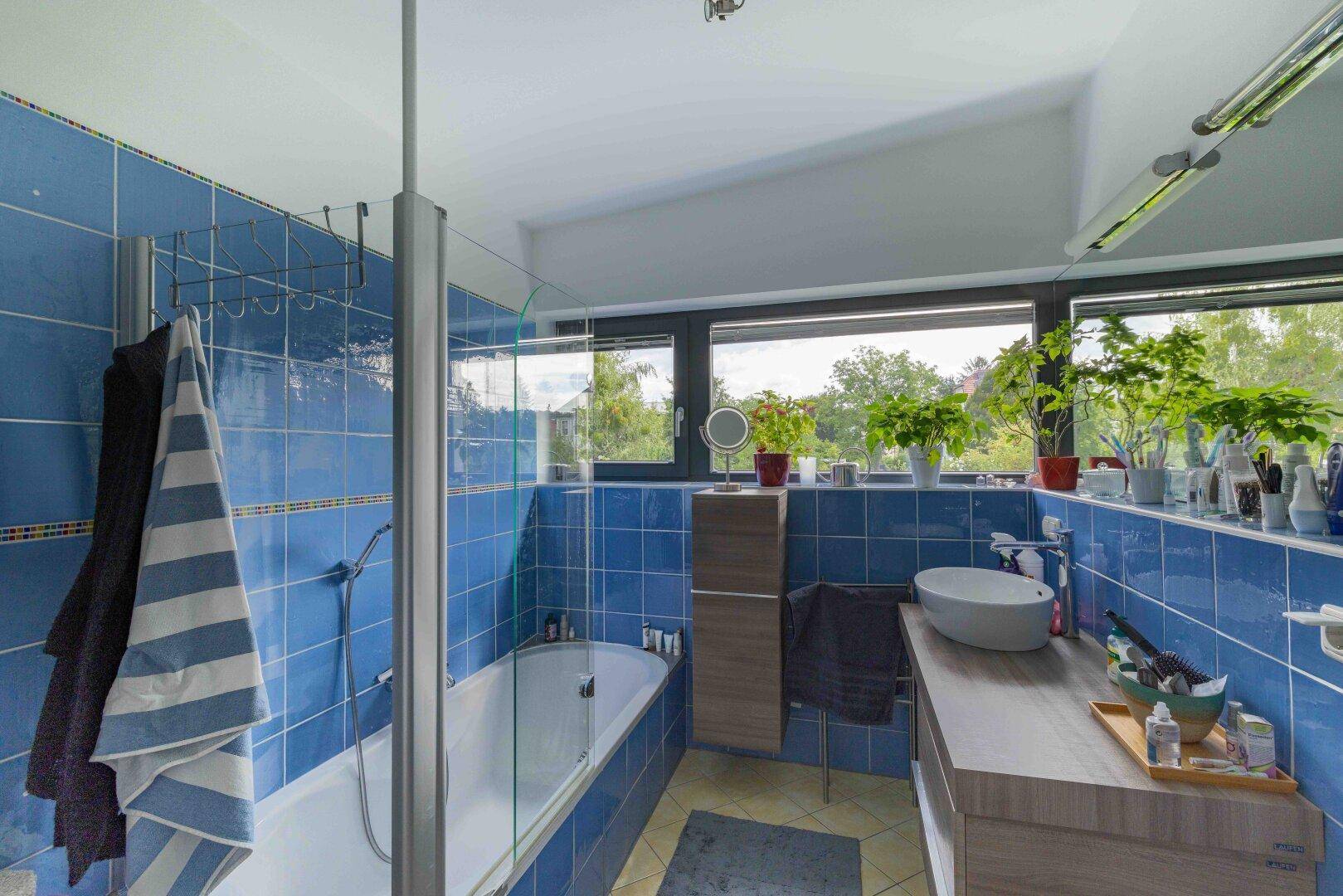 Modernes Badezimmer mit blauen Fliesen, Badewanne und großem Fenster mit viel Tageslicht.
