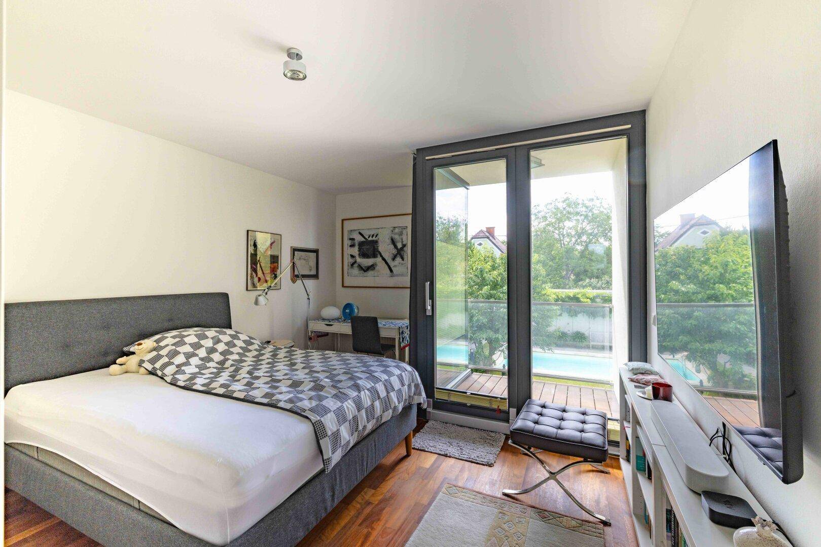 Schlafzimmer mit Doppelbett, Holzboden und Zugang zu einem französischen Balkon mit Poolblick.
