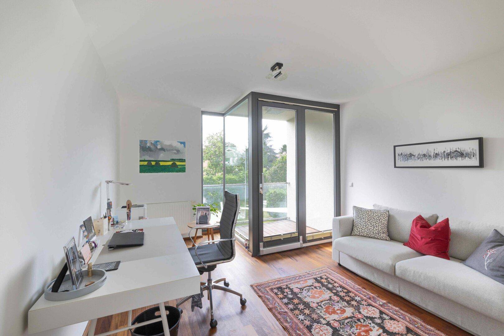 Helles Zimmer mit Schreibtisch, Sofa und Zugang zu einem französischen Balkon.