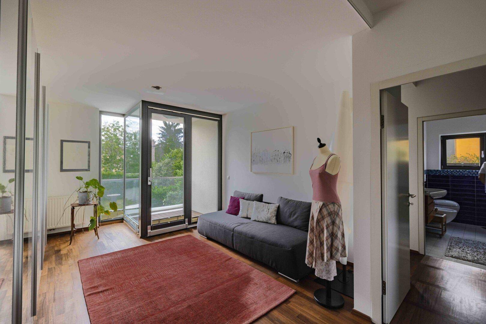 Heller Bereich mit Sofa, Holzboden und Zugang zu einem französischen Balkon und Badezimmer.