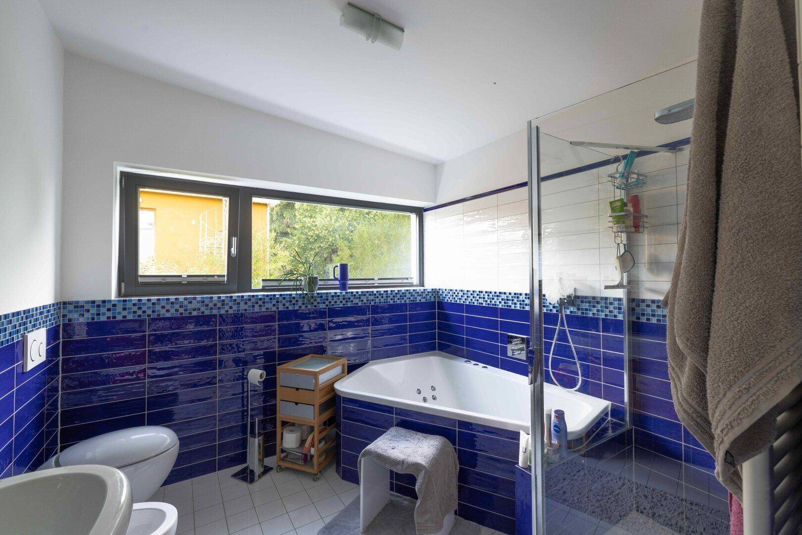 Modernes Badezimmer mit blauen Fliesen, Eckbadewanne mit Whirlpoolfunktion und Bidet.