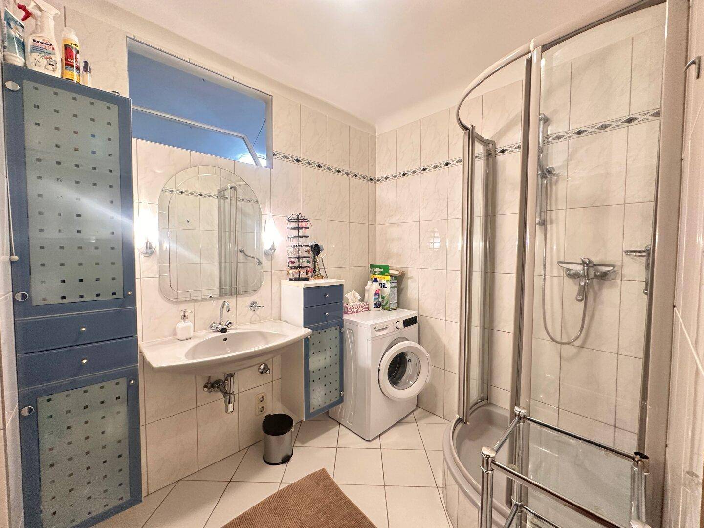 Funktionales Badezimmer mit Duschkabine, Waschbecken, WC und Waschmaschine, hell gefliest.