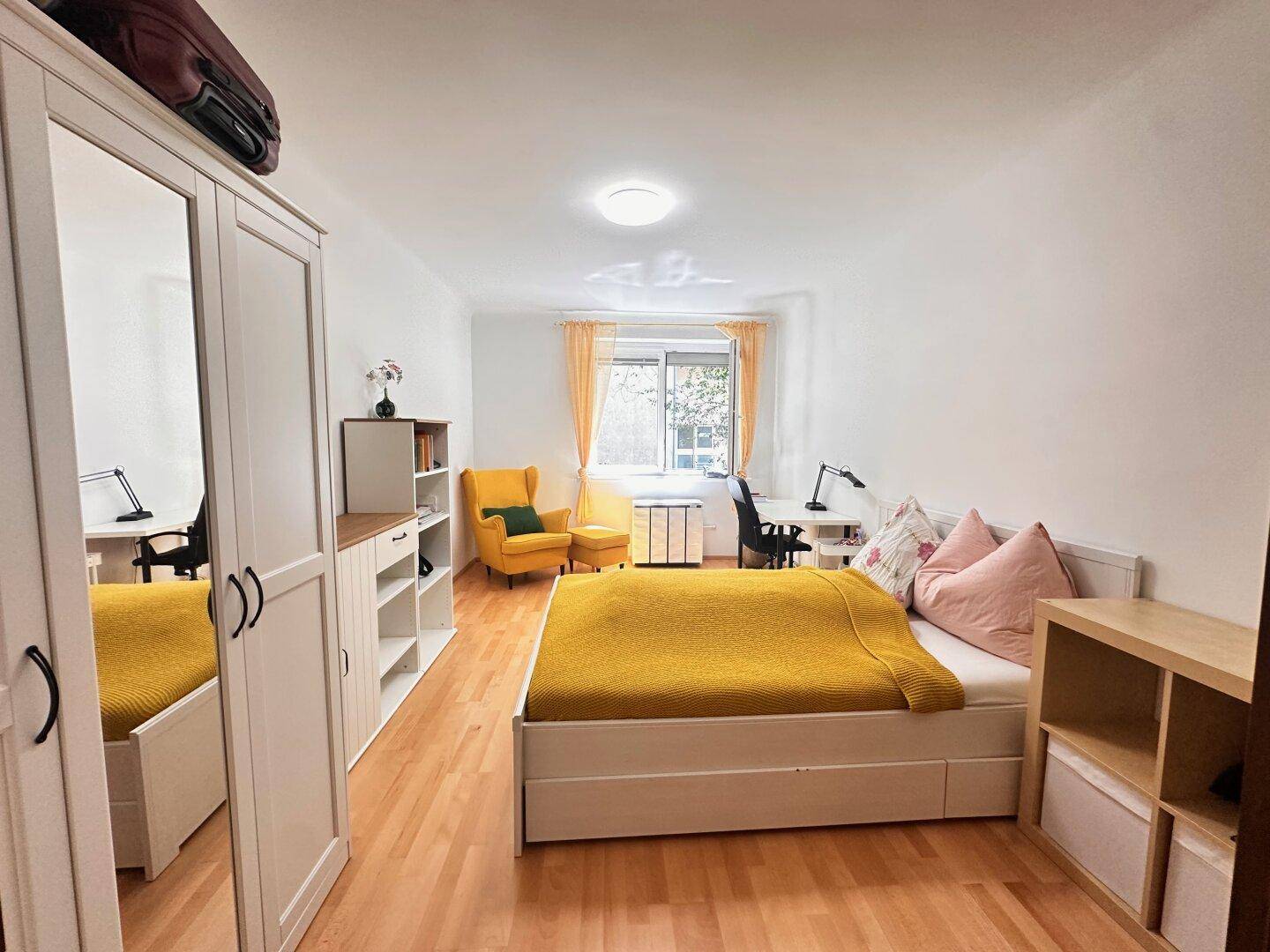 Helles Schlafzimmer mit Holzboden, Bett, Schreibtisch und einem großen Spiegelschrank.