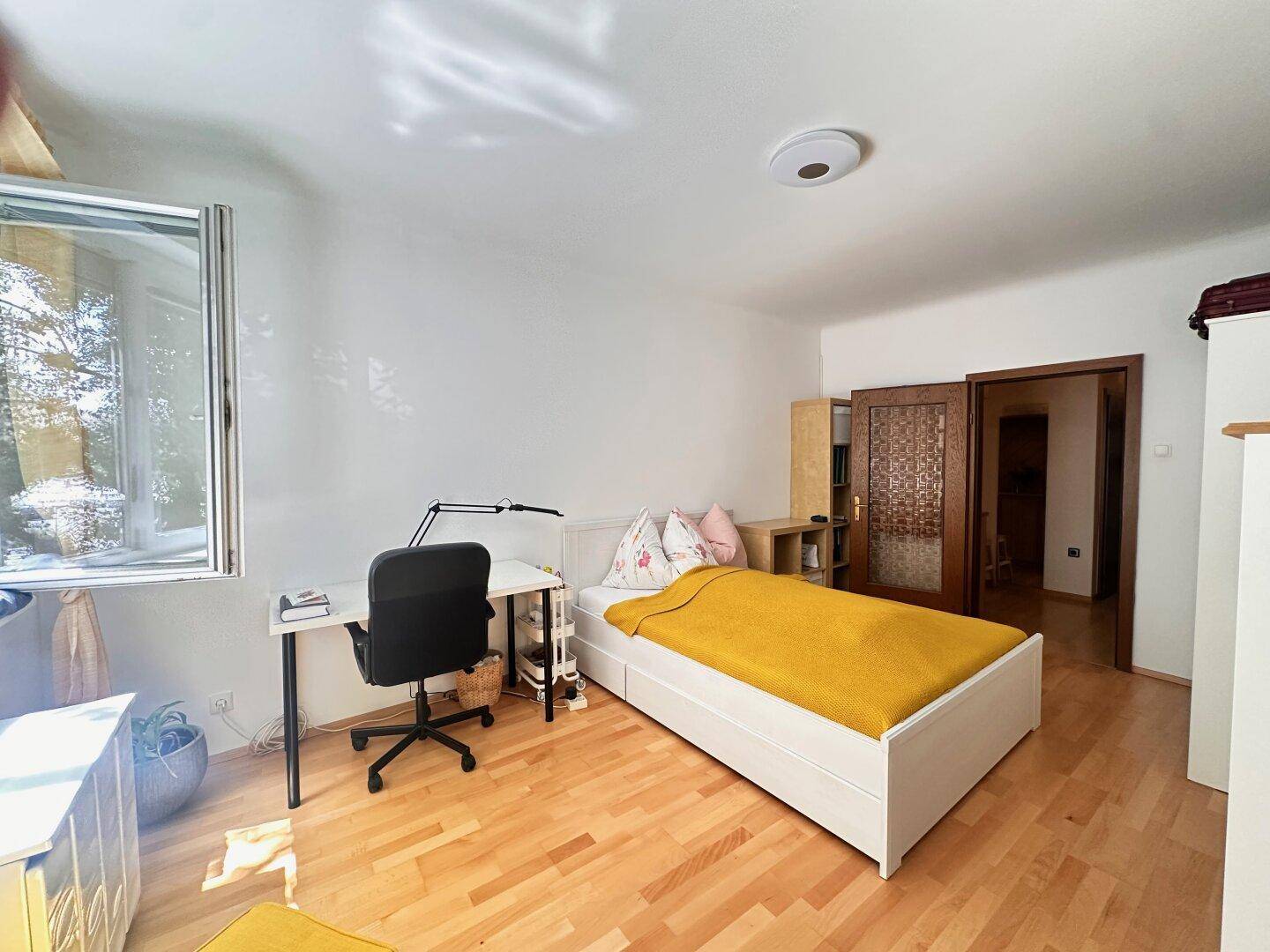 Schlafzimmer mit Holzboden, Schreibtisch und einem schönen Blick aus dem Fenster ins Grüne.