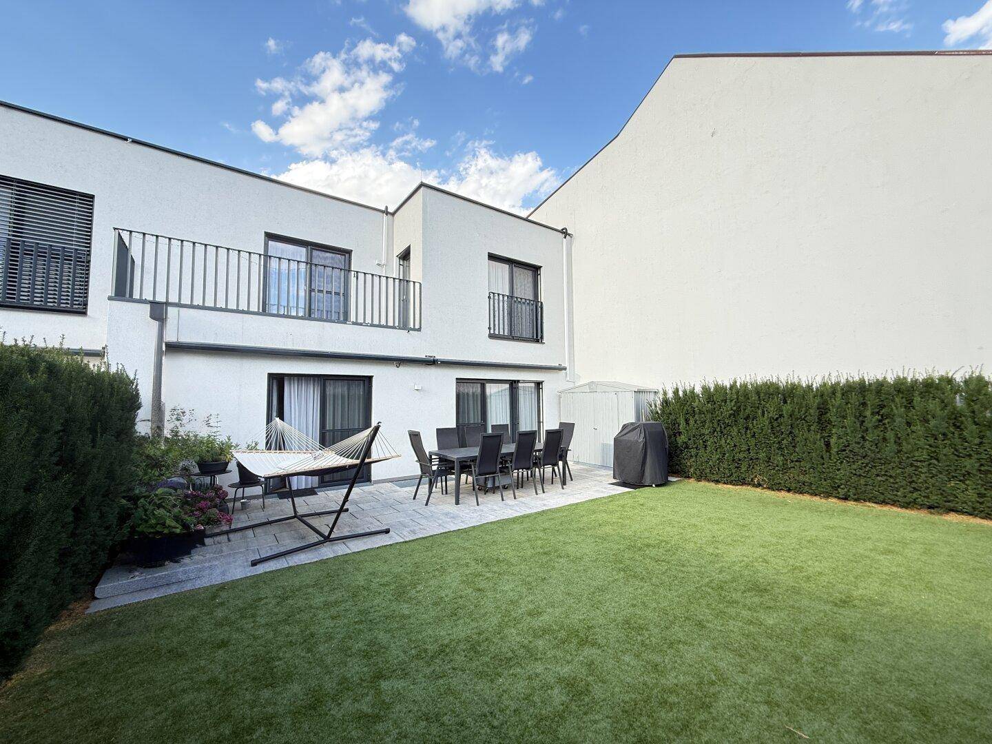 Moderne Hausfassade mit Balkonen und einer großzügigen Terrasse, die in einen gepflegten Garten übergeht.