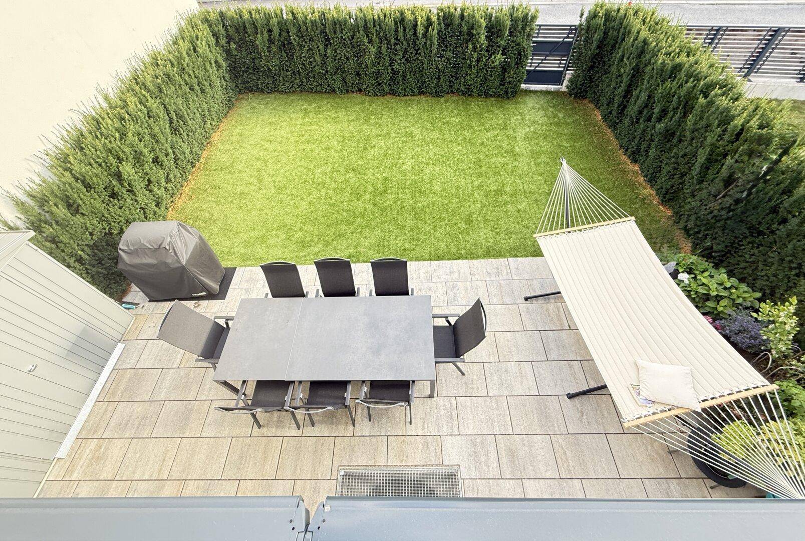 Vogelperspektive auf den privaten Garten mit großer Terrasse, Rasenfläche und Hängematte, umgeben von Hecken.