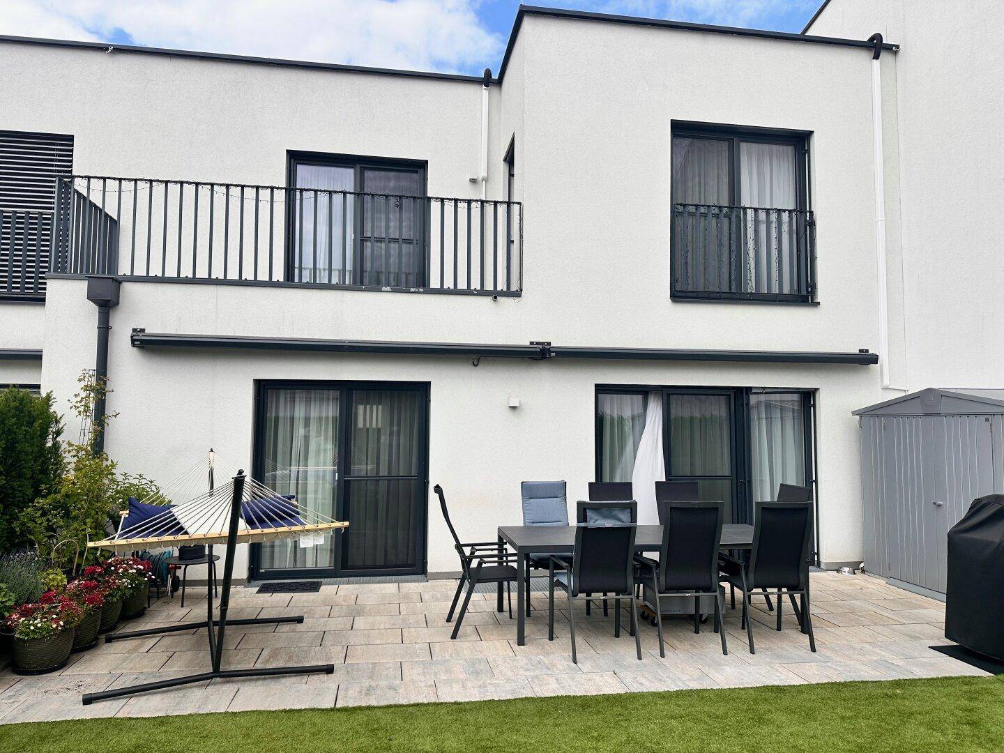 Geräumige Terrasse mit Esstisch und Hängematte, direkt am Haus gelegen und von Grün umgeben.