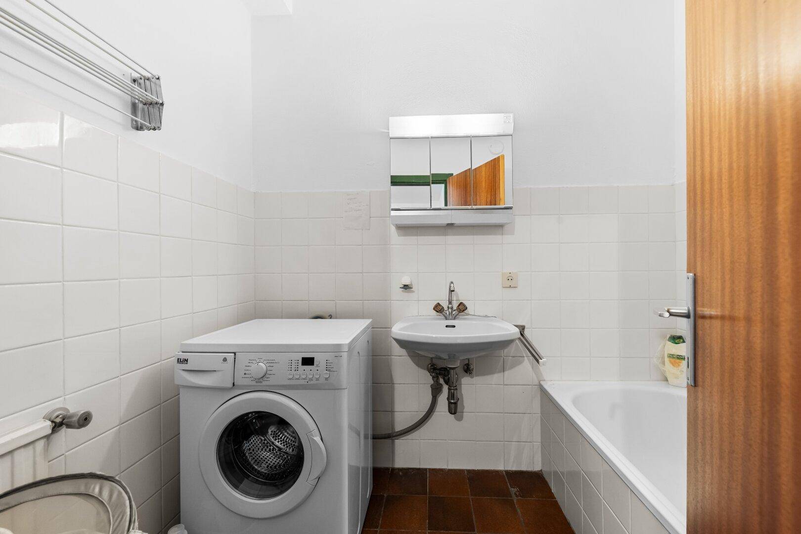 Badezimmer mit Badewanne, Waschbecken, Waschmaschine und weißen Wandfliesen.