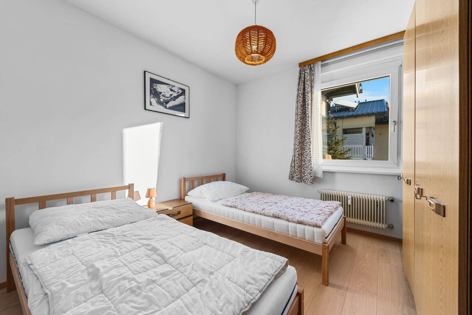 Schlafzimmer mit zwei Einzelbetten, Holzfußboden und einem Fenster mit Blick nach draußen.