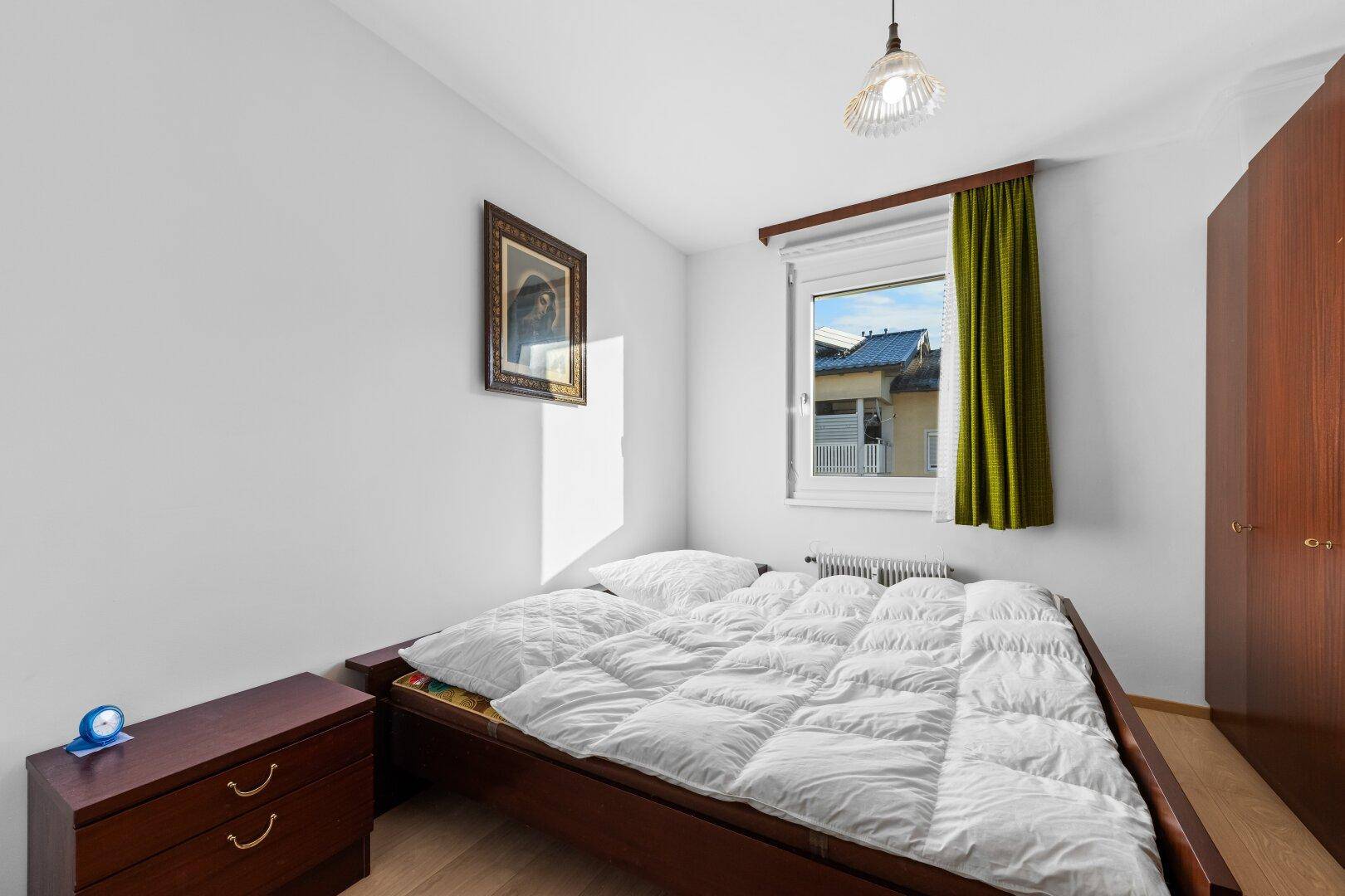 Gemütliches Schlafzimmer mit Doppelbett, Holzfußboden und einem Fenster mit grünem Vorhang.