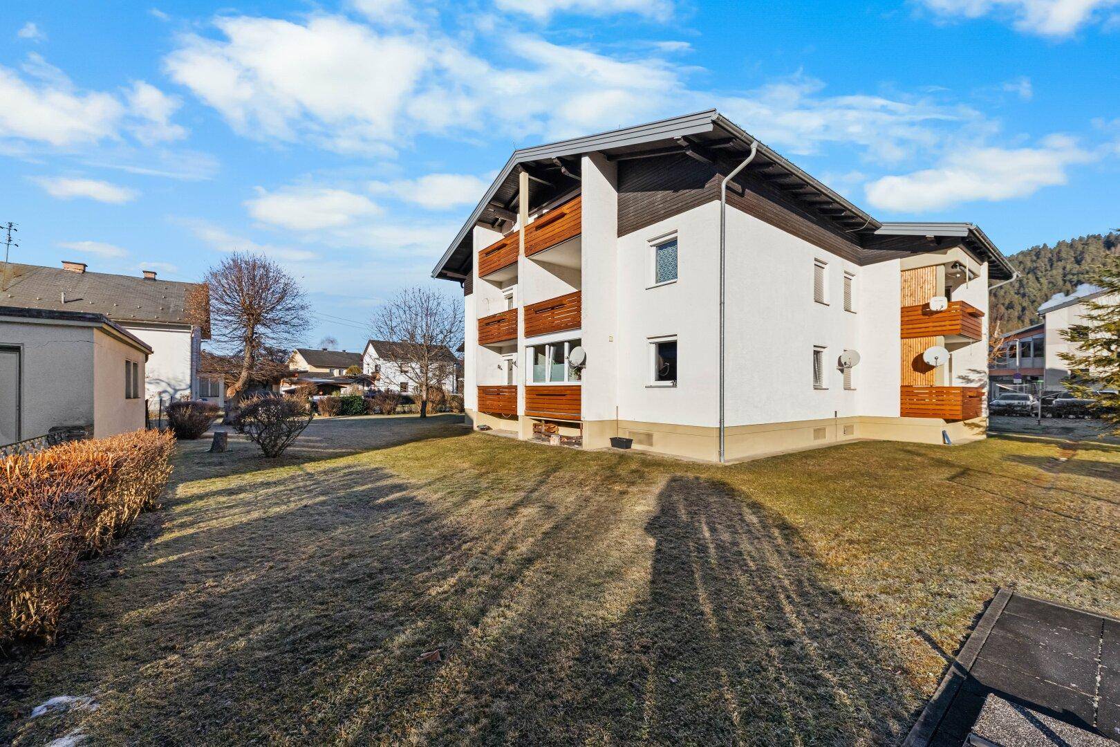 Ansicht des Mehrfamilienhauses mit Balkonen und Rasenfläche an einem sonnigen Wintertag.