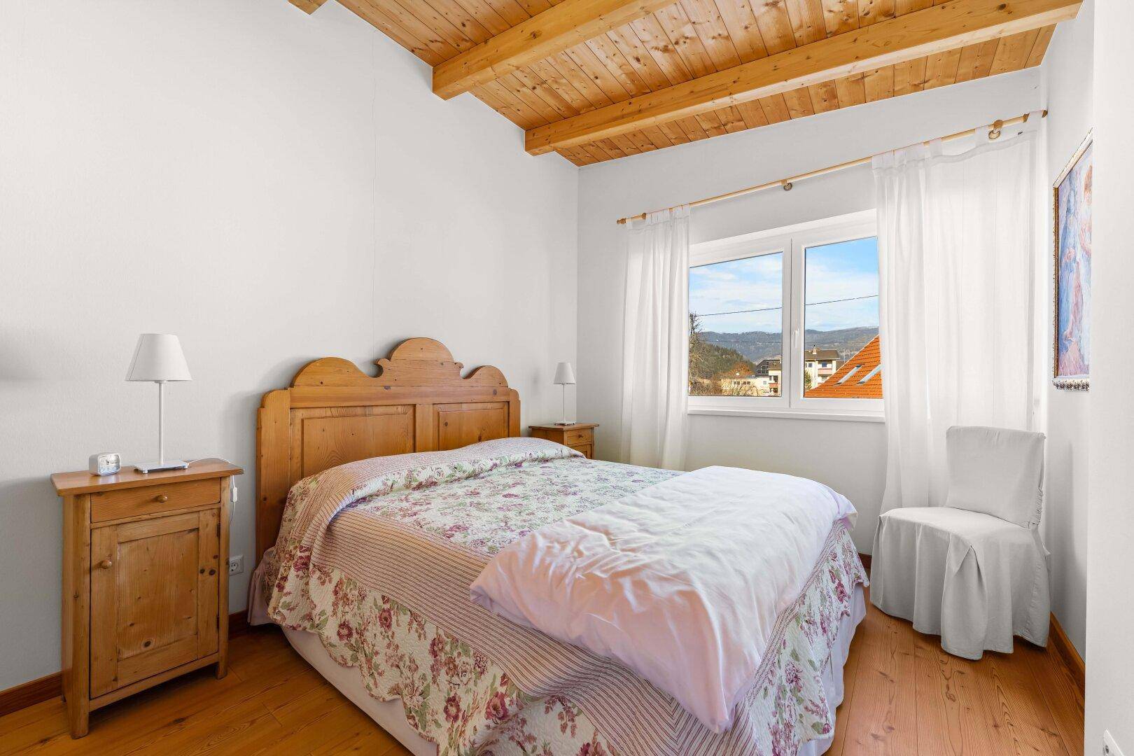 Schlafzimmer mit Holzbett, Holzbalkendecke und Ausblick auf die umliegende Landschaft.
