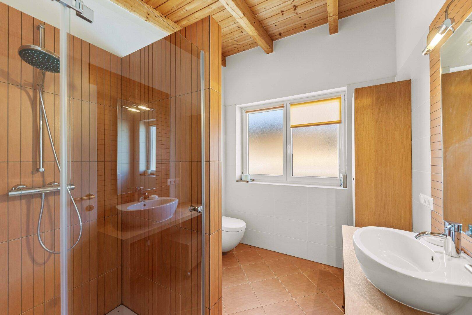Modernes Badezimmer mit Dusche, Doppelwaschbecken und Holzbalkendecke.