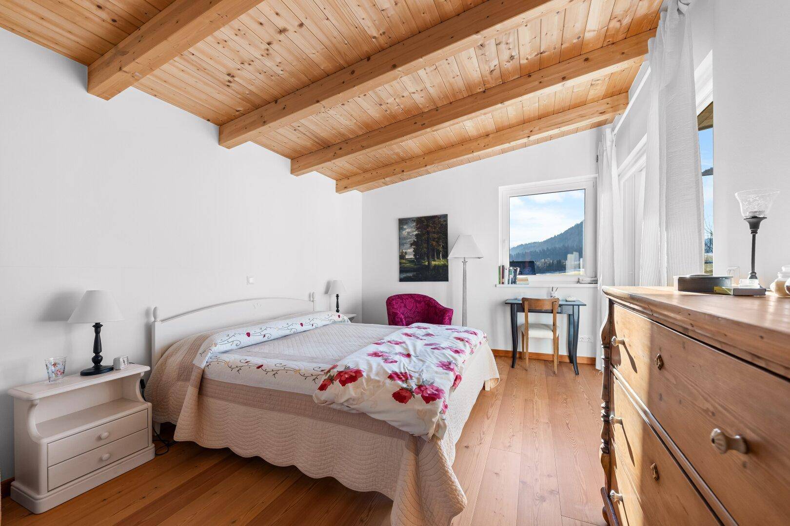 Geräumiges Schlafzimmer mit Holzbalkendecke, Holzboden und Blick ins Grüne.