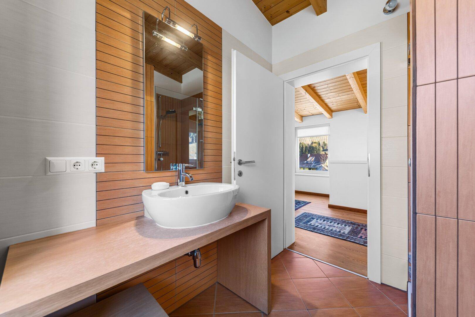 Badezimmer mit modernem Waschbecken, Spiegel und Holzakzenten an der Wand.