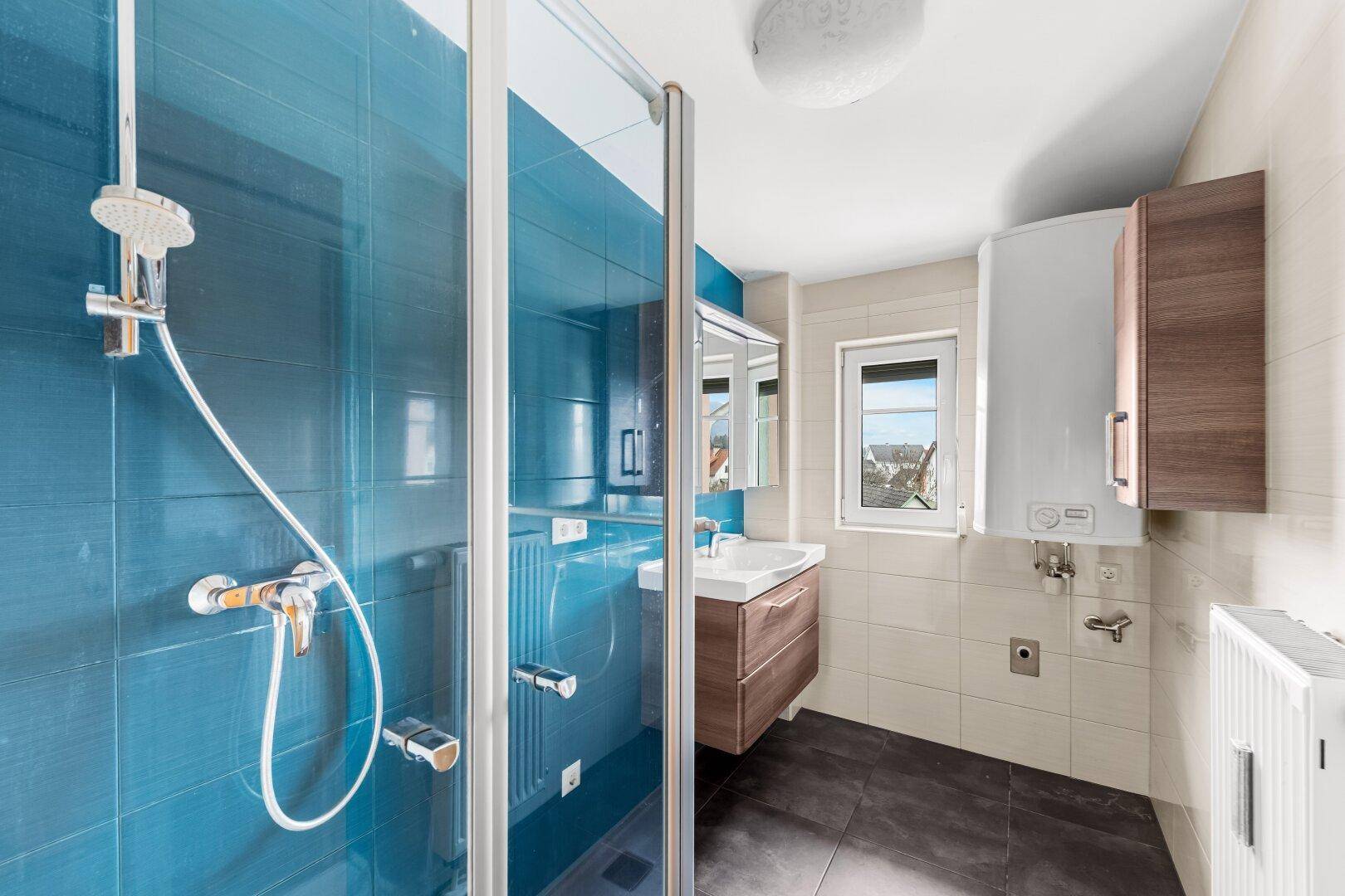 Modernes Badezimmer mit blauen Fliesen in der Dusche und Fenster.