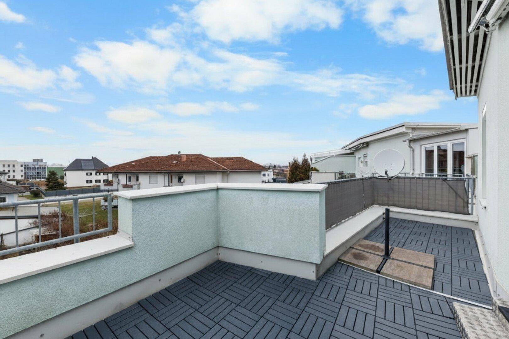 Geräumige Dachterrasse mit grauen Bodenfliesen und Blick auf die Umgebung.