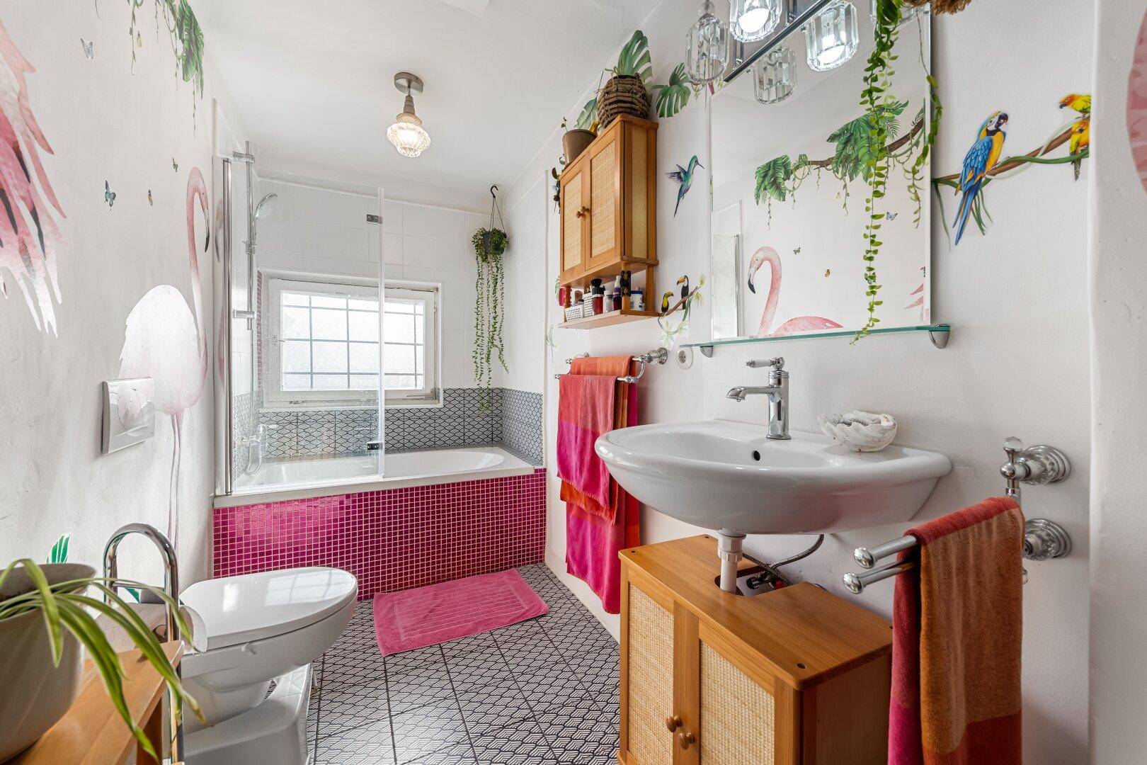 Buntes Badezimmer mit Badewanne, Waschbecken und verspielten Wandmalereien im tropischen Stil.