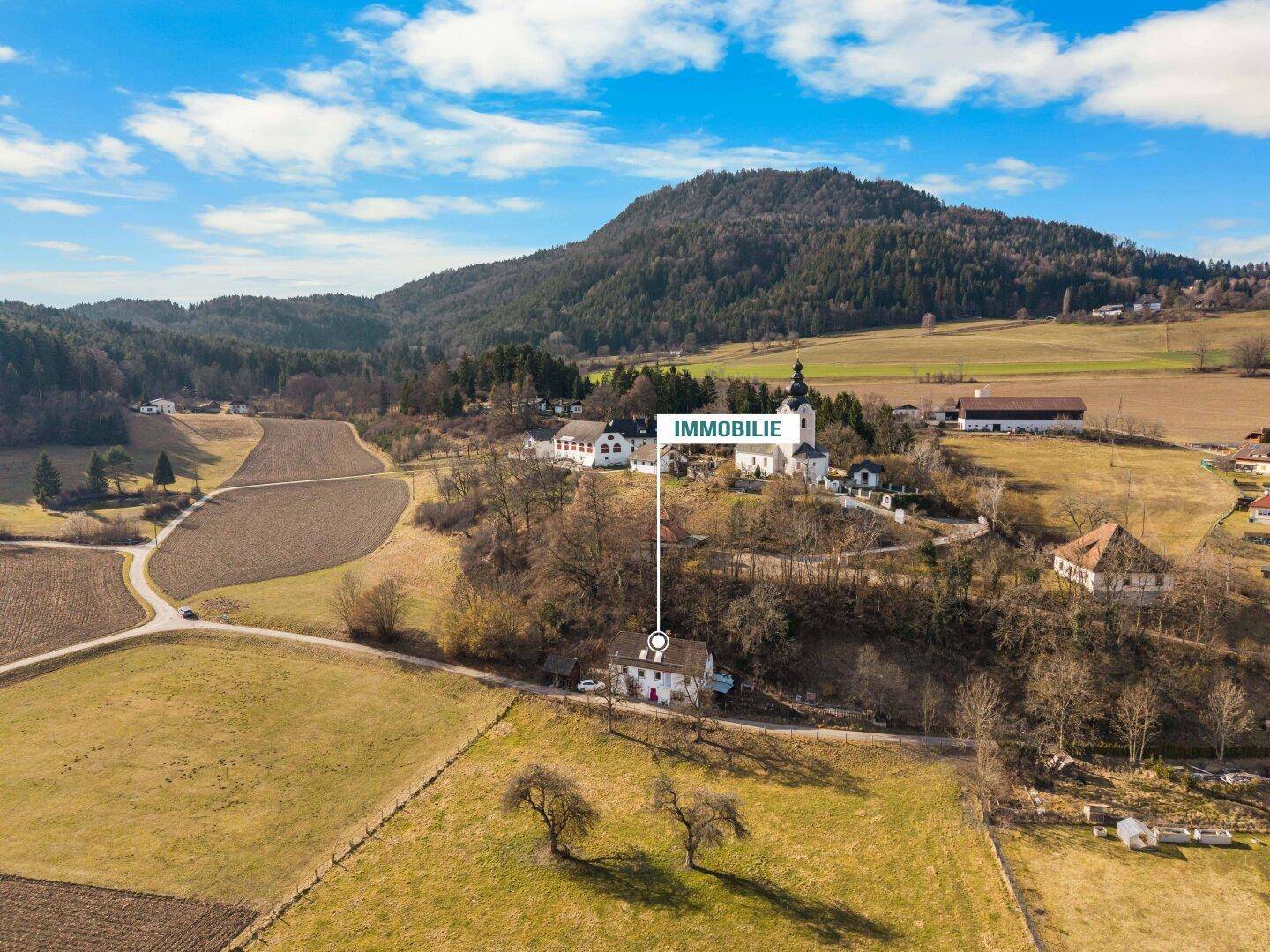 Luftaufnahme des Anwesens in ländlicher Umgebung mit Feldern und bewaldeten Hügeln im Hintergrund.