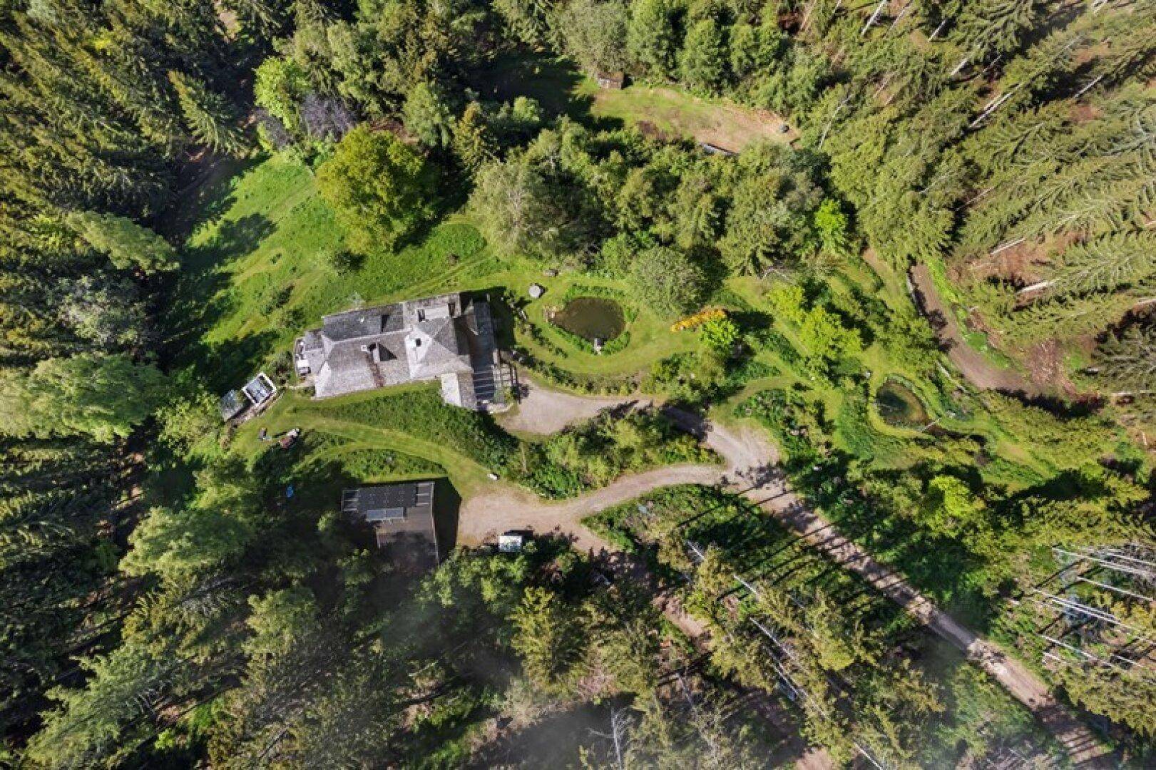 Luftaufnahme des weitläufigen Anwesens, umgeben von dichtem Wald und grünen Wiesen.