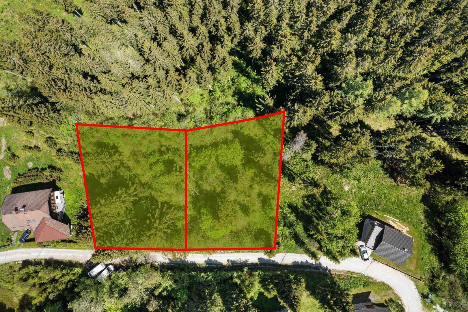 Draufsicht auf zwei markierte Grundstücke, umgeben von Wald und einer Zufahrtsstraße.