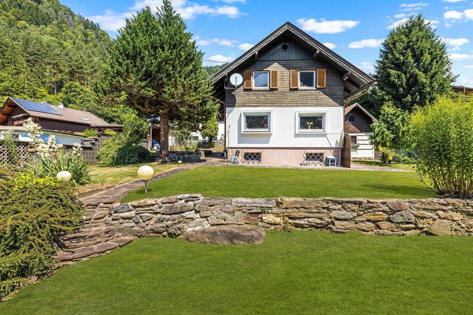 Vorderansicht des Hauses mit gepflegtem Garten, Rasenflächen und traditionellen Fensterläden.