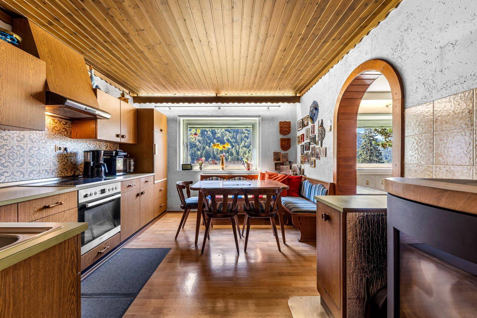 Traditionelle Wohnküche mit Holzelementen, Essbereich und Bergblick durch das Fenster.