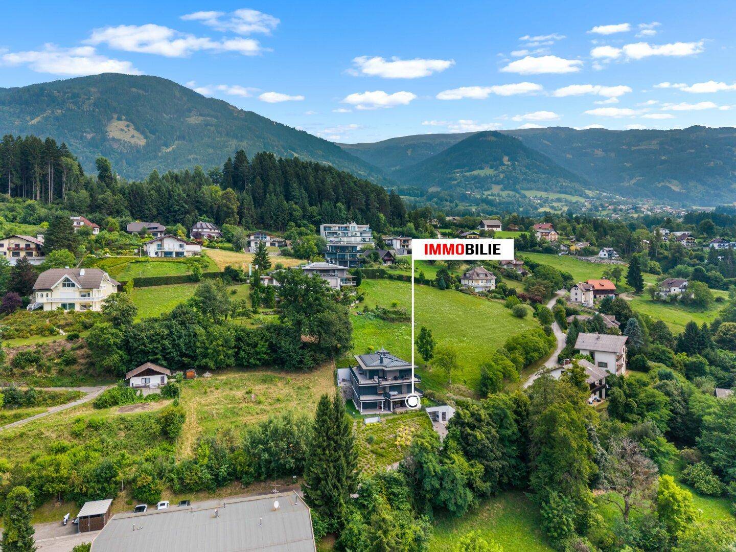 Luftaufnahme eines modernen Gebäudes in einer grünen Hügellandschaft mit Bergblick.