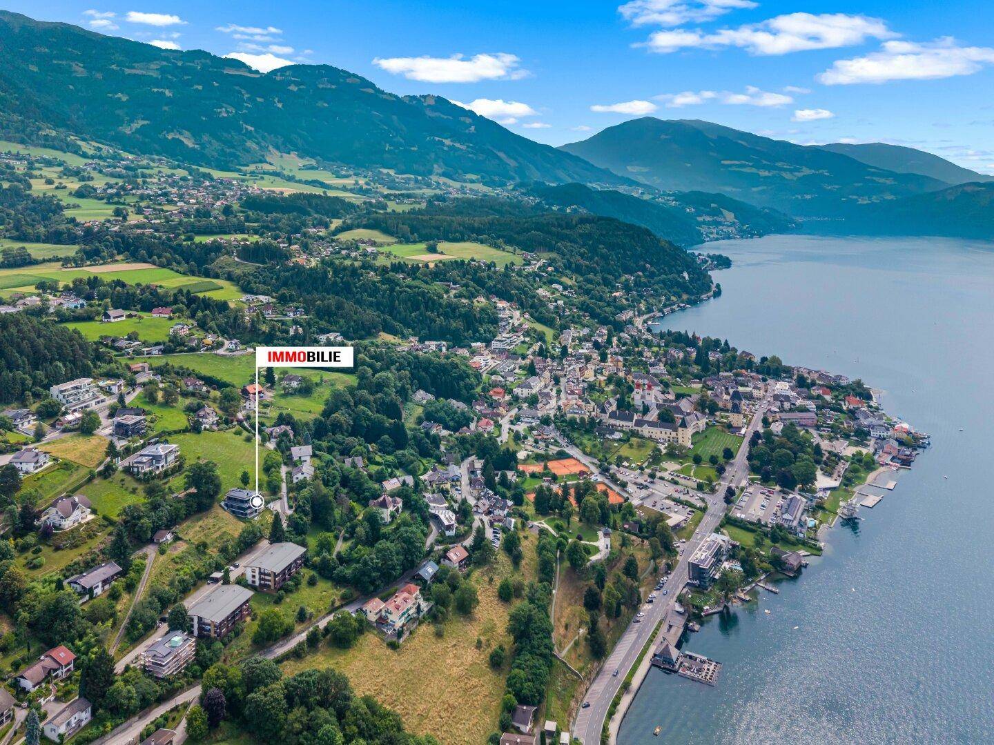Weitläufige Luftaufnahme der Immobilie in einer Siedlung am See mit Bergen im Hintergrund.