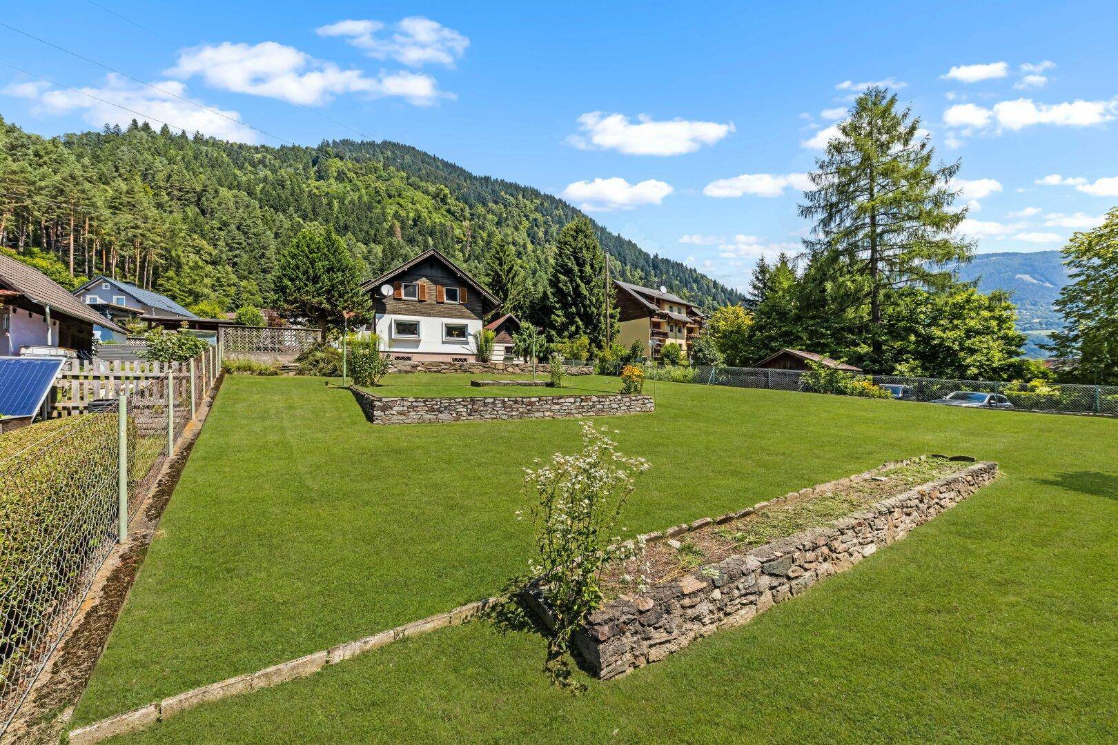 Weitläufiger Garten mit gepflegtem Rasen und Blick auf das Haus und die bewaldeten Hügel.