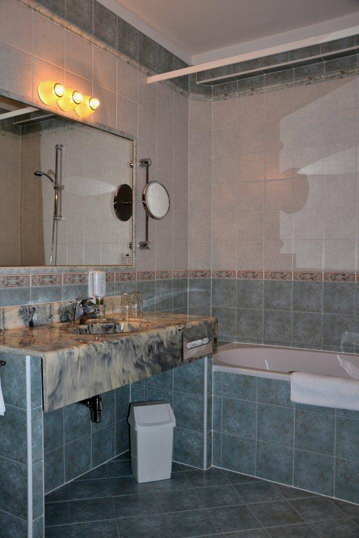 Badezimmer mit Badewanne, Marmorwaschtisch und blaugrauen Fliesen an Wänden und Boden.