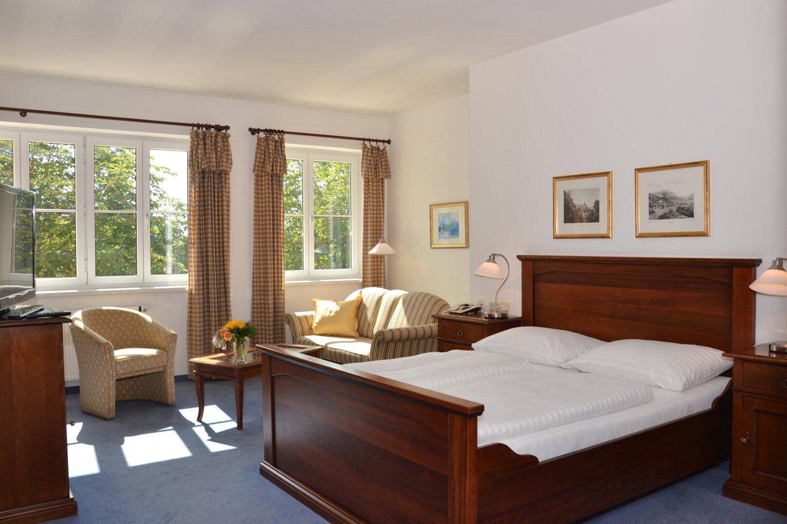 Helles Schlafzimmer mit Doppelbett, Sitzbereich und Blick ins Grüne durch große Fenster.